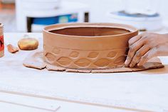 a person is making a clay pot on a table with other pottery items around it