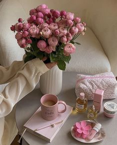 pink flowers in a white vase on a table next to some personal care items and makeup