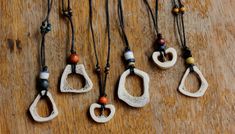 five necklaces with different shapes and colors on a wooden surface, one is made out of ceramic