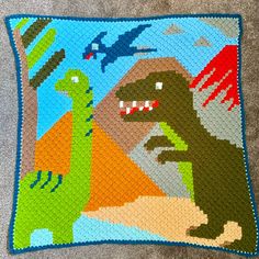 a crocheted dinosaur pillow is shown on the floor, with an image of two dinosaurs