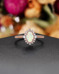 an opal and diamond ring sits on top of a black surface with flowers in the background