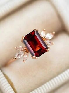 an engagement ring with a large red stone surrounded by small white diamonds in a box