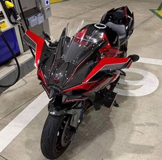 a red and black motorcycle is parked at a gas station with no one around it