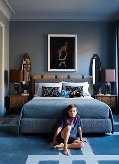 a young boy sitting on the floor in front of a bed with blue carpeting