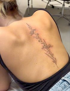 a woman with a tattoo on her back is sitting down and looking at the camera