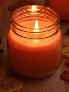 a lit candle sitting on top of a wooden table next to leaves and autumn decorations