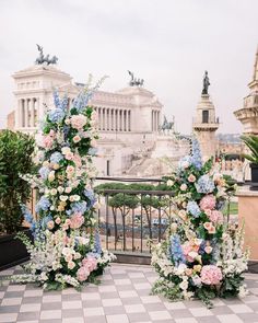 two floral arrangements on the ground in front of an ornate building with statues and columns