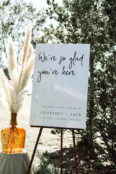 a sign and some white feathers on top of an easel with a wine bottle in it