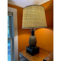 a pineapple lamp sitting on top of a wooden table next to a window with an orange wall