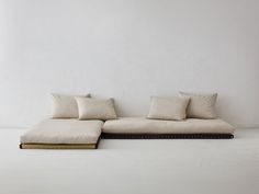 a white couch with pillows on it in front of a white wall and flooring