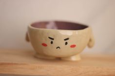 a small bowl sitting on top of a wooden table next to a white wall with red eyes