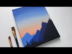 an acrylic painting of mountains and trees with a paintbrush on the table