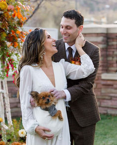 a man and woman standing next to each other holding a small dog in their arms