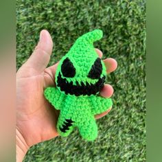 a hand holding a small green crocheted toy with a creepy face on it