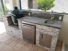 an outdoor kitchen with stainless steel appliances and granite counter tops is shown in front of a large window