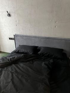 an unmade bed with black sheets and pillows in front of a white brick wall