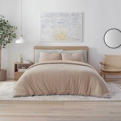 a bedroom with white walls and wooden floors, a bed covered in beige linens