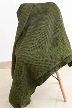 a green blanket sitting on top of a wooden chair next to a white wall and floor