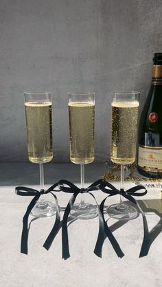 three wine glasses with black ribbon around them next to a bottle and two glasses filled with champagne