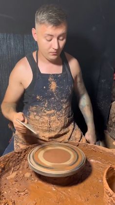 a man sitting in front of a clay pot holding a spoon and pointing at it