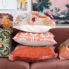 a pile of pillows sitting on top of a brown couch next to pictures and paintings