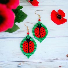 a pair of red and green earrings sitting on top of a white wooden table next to flowers