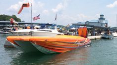 an orange and white boat floating on top of water next to a dock with flags