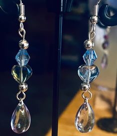 Elevate your style with these exquisite blue iridescent gemstone drop earrings. Each earring features a stunning teardrop gem that captures and reflects light, creating a mesmerizing dance of colors. Adorned with a harmonious blend of iridescent heart and rounded beads, these earrings are finished with elegant silver accents, making them a versatile choice for both casual and formal occasions. Iridescent Drop Earrings With Matching Jewelry, Iridescent Drop Earrings With Matching Jewelry Set, Iridescent Jewelry With Matching Drop Earrings, Iridescent Drop Earrings Jewelry Set, Iridescent Pierced Drop Earrings, Elegant Iridescent Crystal Jewelry, Iridescent Drop Earrings For Jewelry Making, Elegant Iridescent Drop Jewelry, Party Jewelry With Iridescent Ear Wire