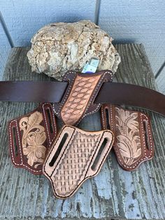 three leather holsters sitting on top of a wooden bench next to a rock and stone