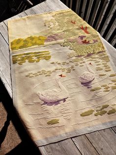 a table with a wooden chair and an old rug on it that has swans in the water