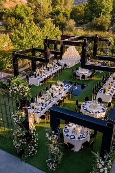 an outdoor dining area with tables and chairs set up in the grass, surrounded by greenery