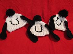 two knitted hats with faces on them sitting on a red surface, one has black and white pom - poms