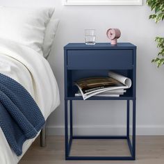 a blue nightstand with magazines on it next to a bed