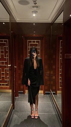 a woman in a black dress is looking at her cell phone while standing in an elevator