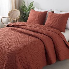 an orange quilted bedspread and pillows on a bed with a chair in the background