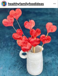 some heart shaped lollipops are in a white cup on a blue surface