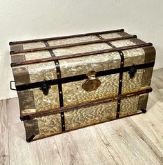 an old trunk is sitting on the floor in front of a white wall and wooden floors