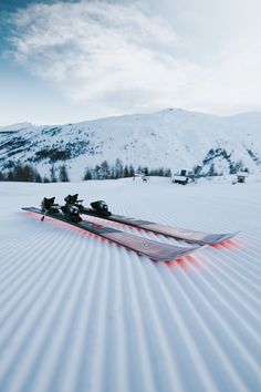 a pair of skis laying on top of snow covered ground next to a mountain