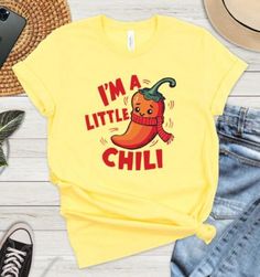 This adorable "I'm a Little Chili" T-shirt features a cute cartoon chili pepper with a playful expression, making it the perfect addition to your casual wardrobe. Made from soft, breathable fabric, this yellow tee combines comfort with a fun sense of style. Ideal for chili enthusiasts, foodies, or anyone looking to add a splash of personality to their outfit. Wear it to parties, gatherings, or just lounging at home. A great gift for friends and family who love a little spice in their life! Product Features: Fabrication: 100% Airlume combed and ring-spun cotton, 32 single 4.2 oz. (Ash - 99% Airlume combed and ring-spun cotton, 1% poly) Seams: Side-seamed Fit: Retail Fit Sizing: Unisex Sizing Label: Tear away label Casual Tops With Funny Text For Gifts, Casual Yellow T-shirt As A Gift, Pun Shirts, Yellow Tees, Red Chili, Funny Graphics, Chili Pepper, Casual Wardrobe, Shirt Price