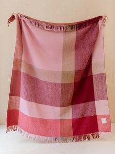 a pink and red checkered blanket with fringes on the bottom, sitting against a wall