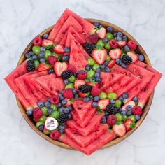 a bowl filled with watermelon, grapes and strawberries on top of a marble counter