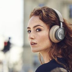 a woman with red hair wearing headphones in front of a building and looking off to the side