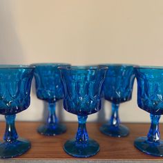 five blue glass goblets sitting on top of a wooden table next to each other