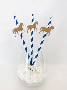 three straws with horses on them are in a vase filled with shredded white paper