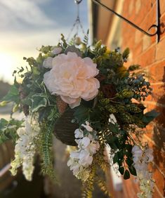 a hanging basket with flowers and greenery on the side of a brick building at sunset