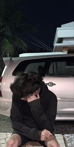 a woman sitting on the ground next to a white car at night with her head in her hands