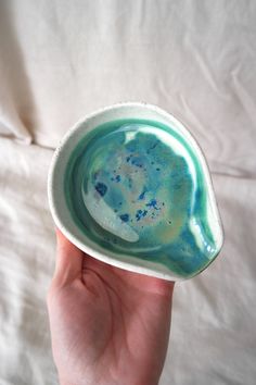 a hand holding a small bowl with blue and green paint