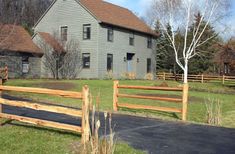 a large gray house sitting on top of a lush green field next to a wooden fence