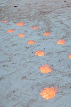 many lit candles in the sand with water around them