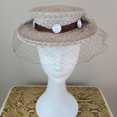 Brand: College Miss Hats  Size: 23 (see measurements) Color: ecru/brown/cream  Fabric Content: straw/tulle/ plastic    Features: You couldn't help but have a good time in this hat. Monochromatic color scheme with a chocolate brown grosgrain ribbon hat band, ecru hat and white buttons around the band. Sweet and fun. The netting is in great condition.    Measurements: Crown Circumference: 18in  Height: 2in  Brim:2 ½ in Strap Length:   Condition: Very good vintage condition. This hat was decommissioned from a museum's collection and has been well-preserved.   Care: spot clean only  Vintage sizing varies. Please check your measurements thoroughly and ask any questions before your purchase. No returns or exchanges. Condition is noted in the product description and can be observed using the zoom Cream Straw Boater Hat For Kentucky Derby, Fitted Retro Cream Hat, Retro Fitted Cream Hat, Retro Cream Hat, Vintage Beach Visor Hat, Cream Straw Boater Hat With Short Brim, Vintage Beige Fascinator With Curved Brim, Vintage Adjustable Beige Fascinator, Vintage Visor Hats For Summer